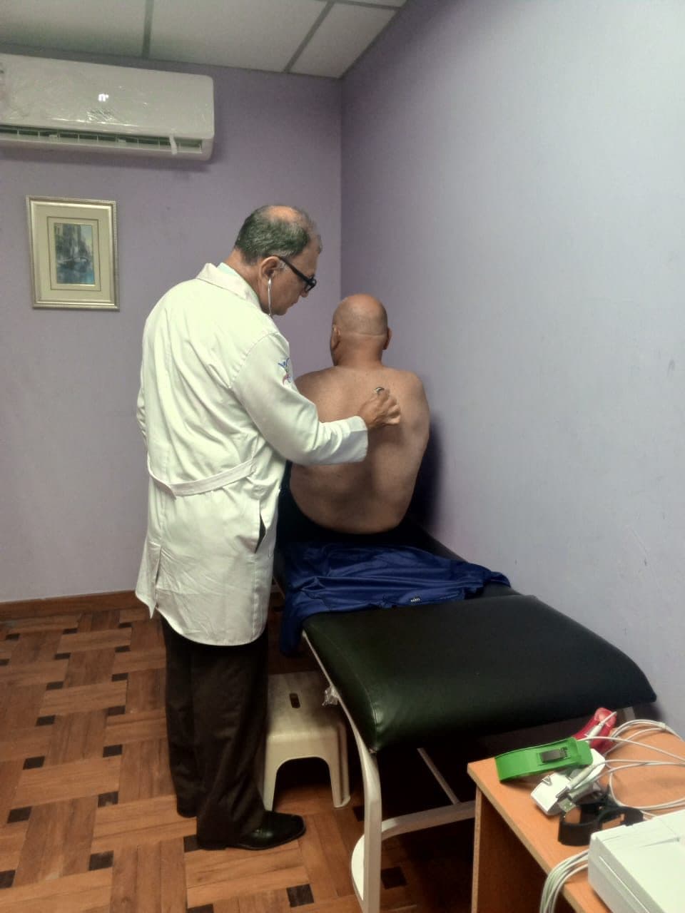 El Dr. Iván López auscultando con el estetoscopio la espalda de un paciente sentado en la camilla del consultorio