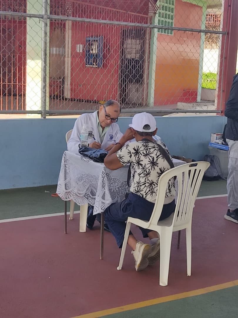 El Dr. Iván López atendiendo a un paciente, sentados a una mesa al aire libre durante una jornada de salud